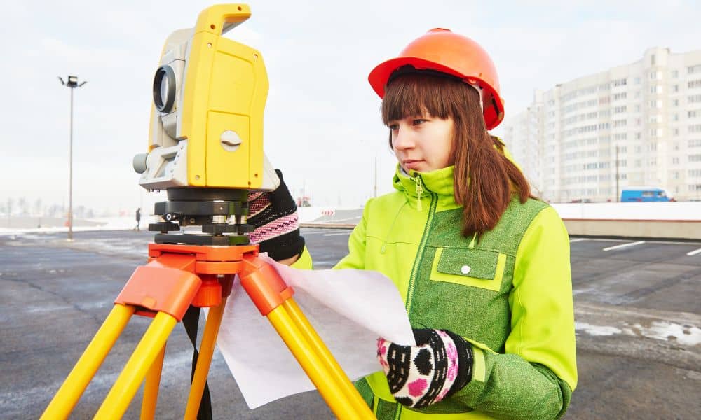 Surveyor using a total station while reviewing field notes for an ALTA title survey on a commercial site
