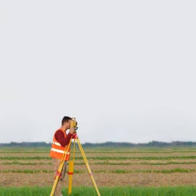 Surveyor using total station equipment in the field performing an ALTA survey to verify property boundaries
