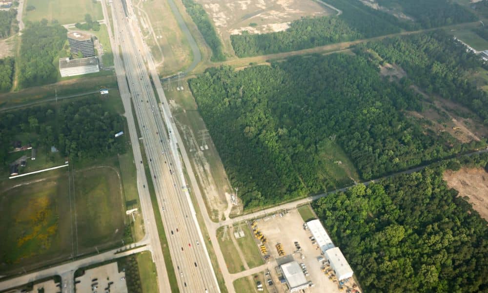 Aerial view showing undeveloped land next to a highway and nearby development, illustrating why an ALTA title survey helps buyers understand surrounding land use risks